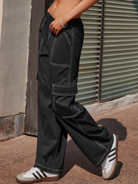 Person wearing black cargo pants and Adidas sneakers standing against a wall.