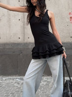 Woman wearing a black peplum top and light blue pants against a concrete wall.