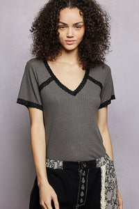 Woman wearing a gray top with black lace trim against a plain background