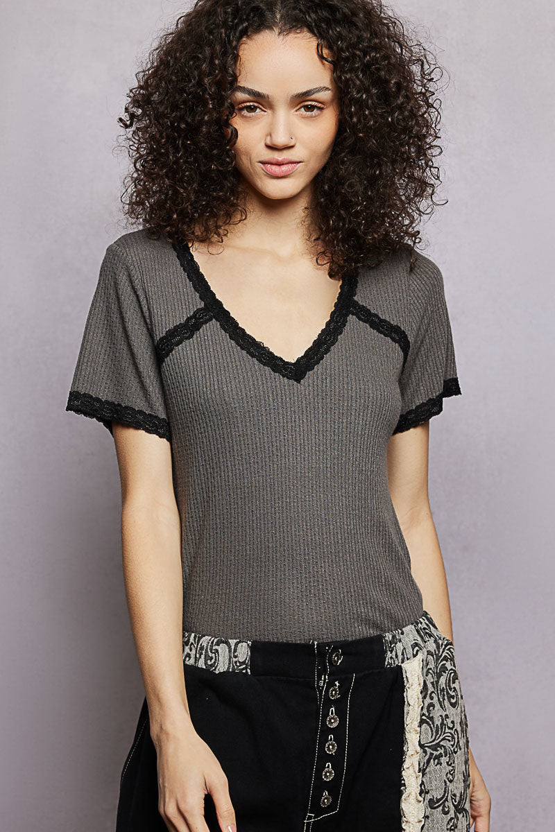Woman wearing a gray top with black lace trim against a plain background