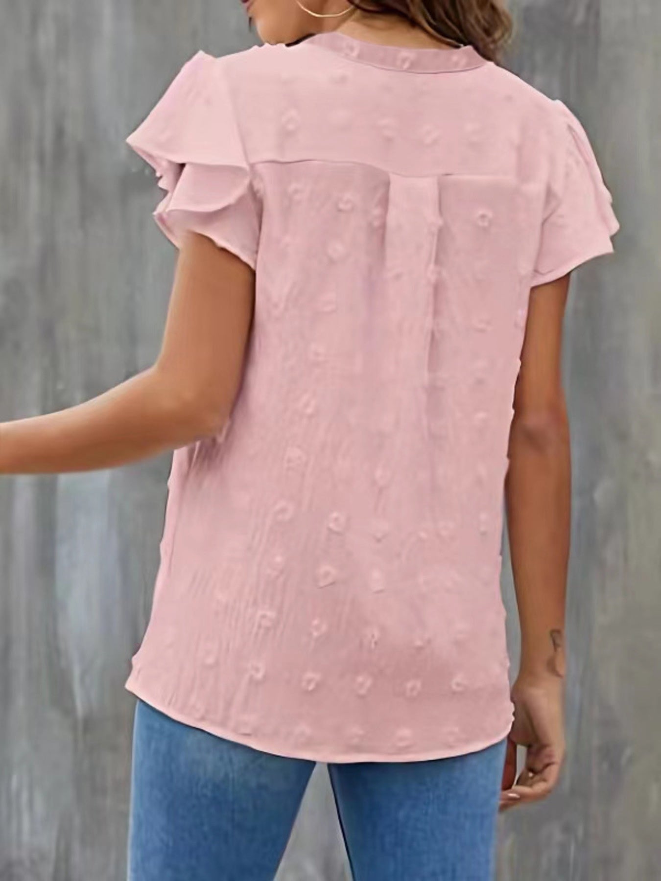 Person wearing a pink blouse with ruffled sleeves against a gray background