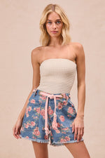 Woman wearing a strapless top and floral shorts on a beige background