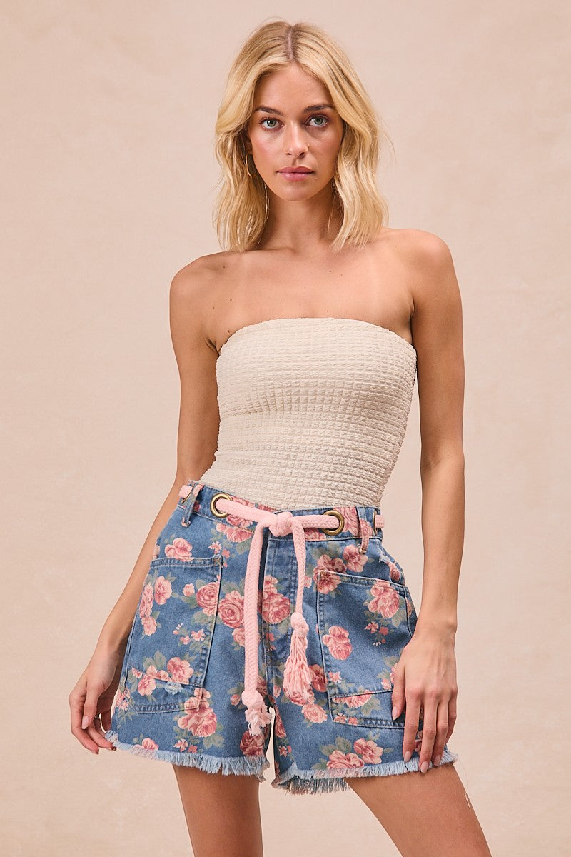 Woman wearing a strapless top and floral shorts on a beige background