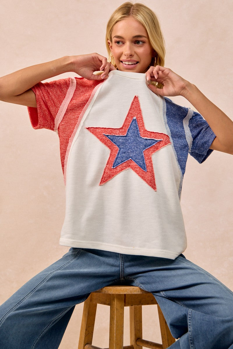 Person wearing a colorful star-patterned shirt sitting on a stool against a beige background