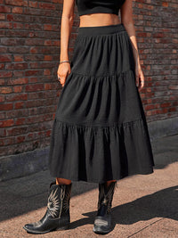 Person wearing a black tiered skirt and cowboy boots against a brick wall.