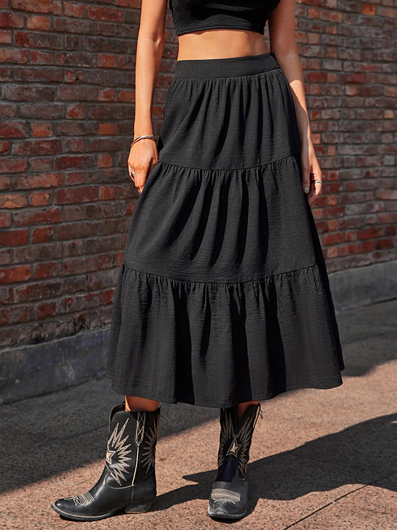 Person wearing a black tiered skirt and cowboy boots against a brick wall.