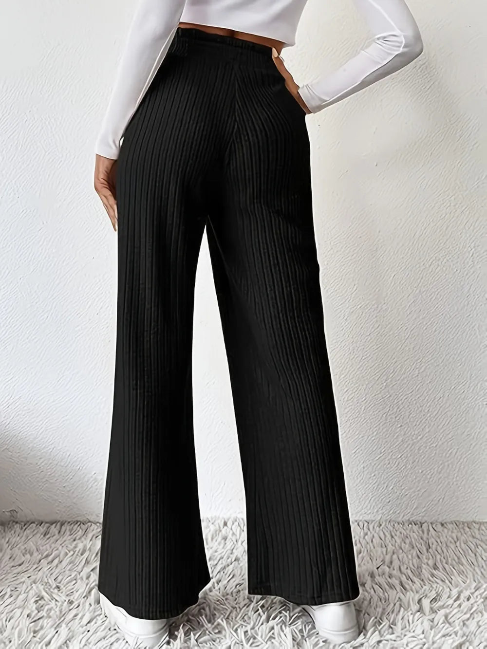 Person wearing black ribbed wide-leg pants with a white shirt on a light background