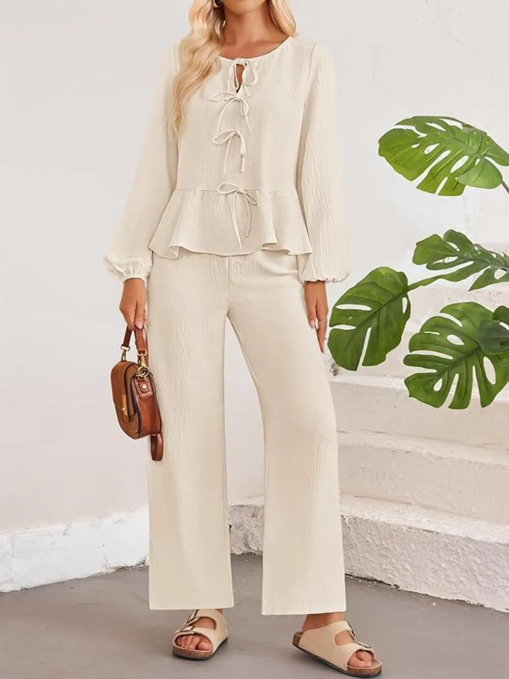 Woman wearing a beige outfit with a plain background and green leaves.