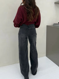 Person wearing a burgundy top and black jeans standing against a plain wall.