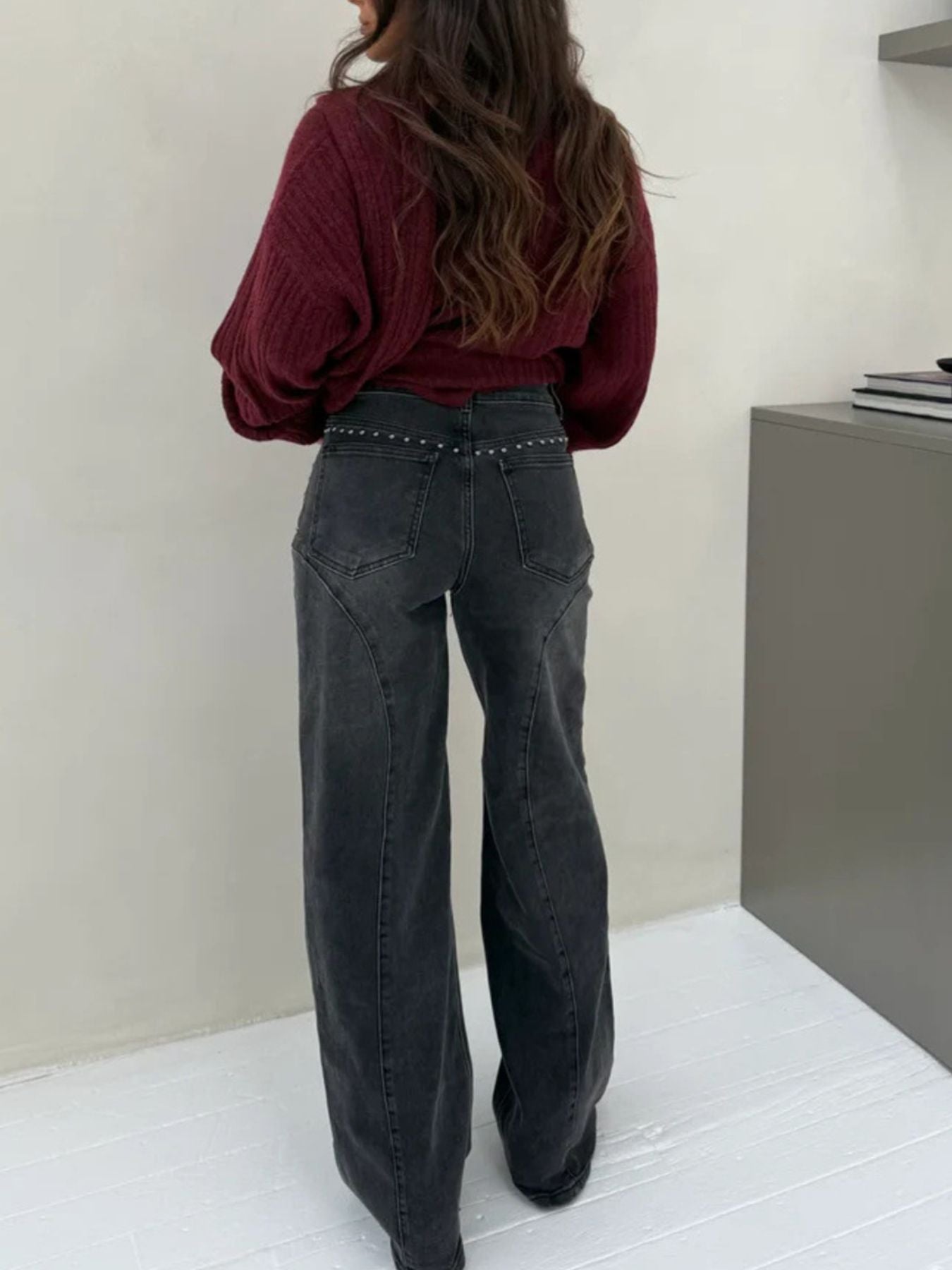 Person wearing a burgundy top and black jeans standing against a plain wall.