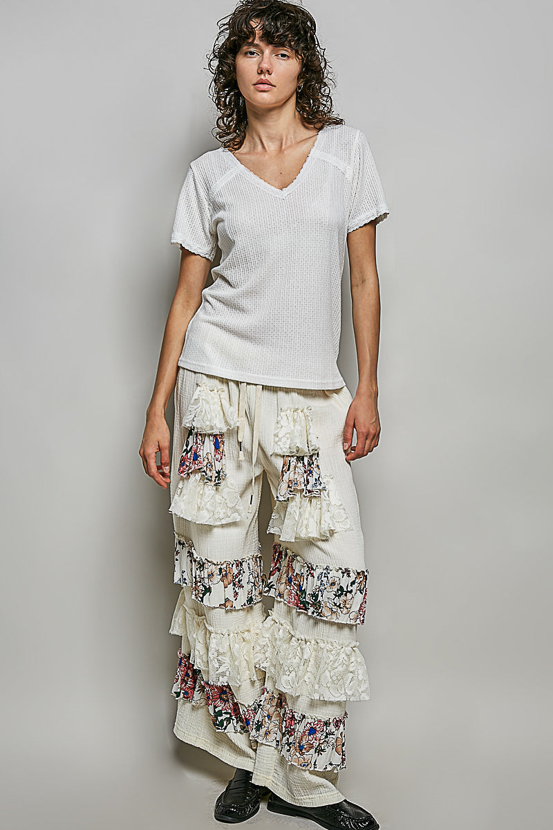 Woman wearing a white top and floral tiered pants against a plain background