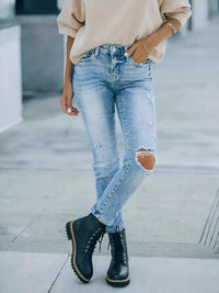 Person wearing distressed blue jeans and black boots on a blurred background