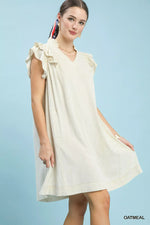 Woman wearing a light-colored dress with ruffled sleeves against a light blue background