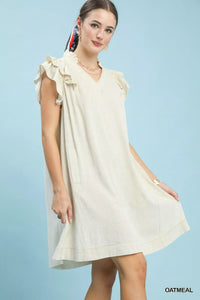 Woman wearing a light-colored dress with ruffled sleeves against a light blue background