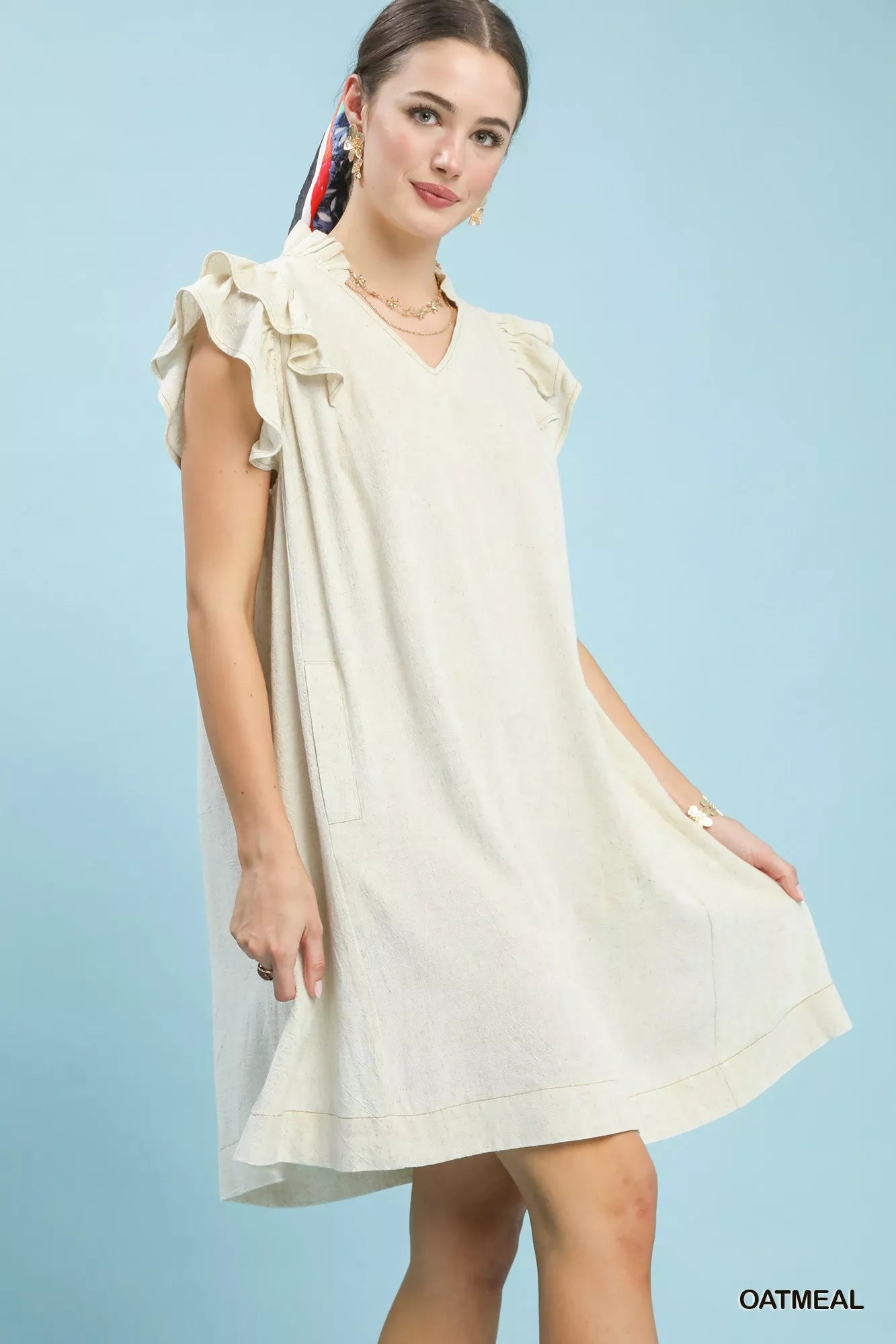 Woman wearing a light-colored dress with ruffled sleeves against a light blue background