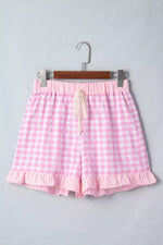 Pink gingham shorts on a hanger against a gray background