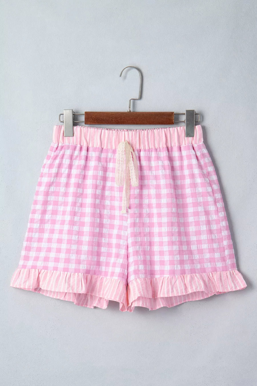 Pink gingham shorts on a hanger against a gray background