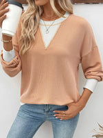 Woman wearing a beige sweater and blue jeans, holding a white cup.