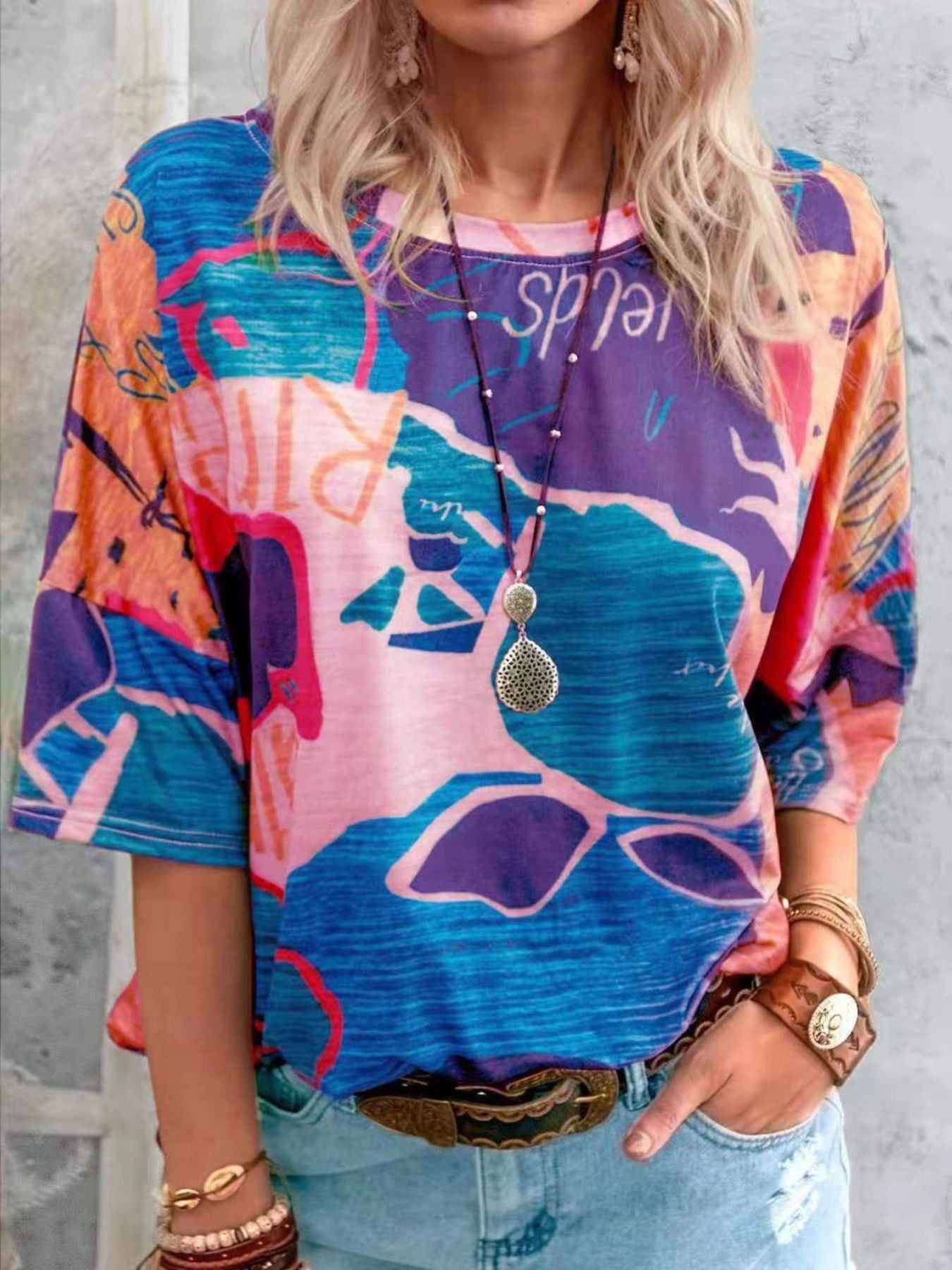 Person wearing a colorful graphic t-shirt with a necklace and bracelets on a gray background