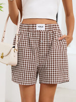 Person wearing brown and white checkered shorts with a white top and beige handbag on a light background