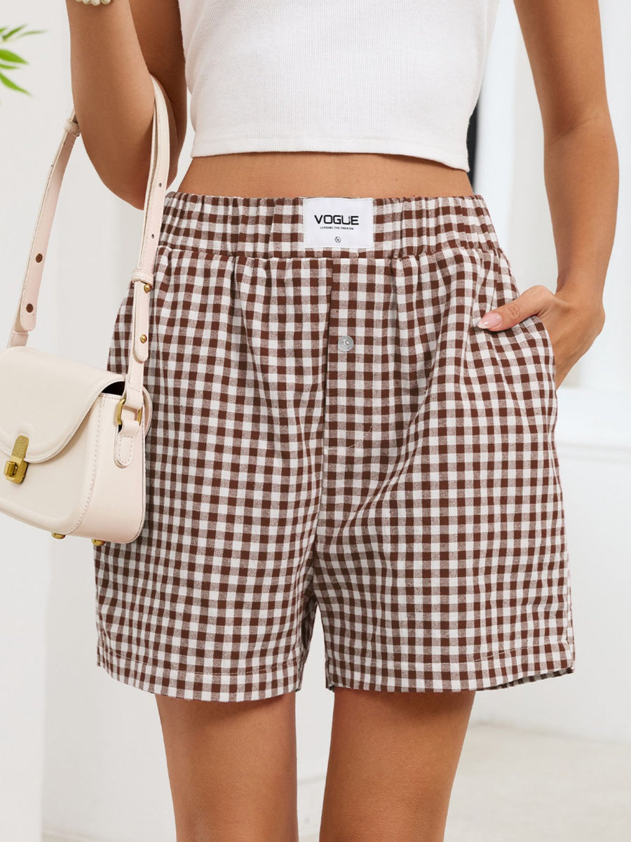 Person wearing brown and white checkered shorts with a white top and beige handbag on a light background