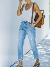 Person wearing a white tank top, blue jeans, and brown sandals with a brown backpack.