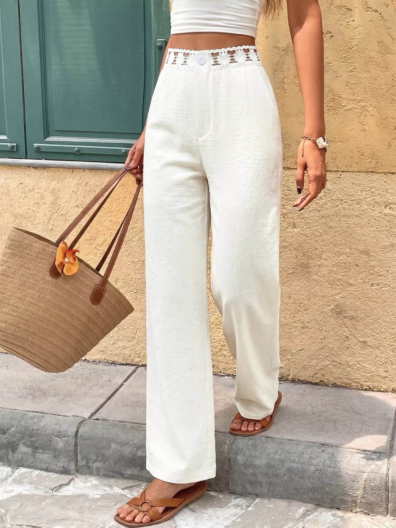 Person wearing white pants and a white top, holding a brown bag on a stone pavement.