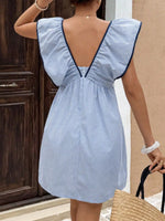 Woman wearing a blue and white striped dress with ruffled sleeves, standing against a neutral wall.