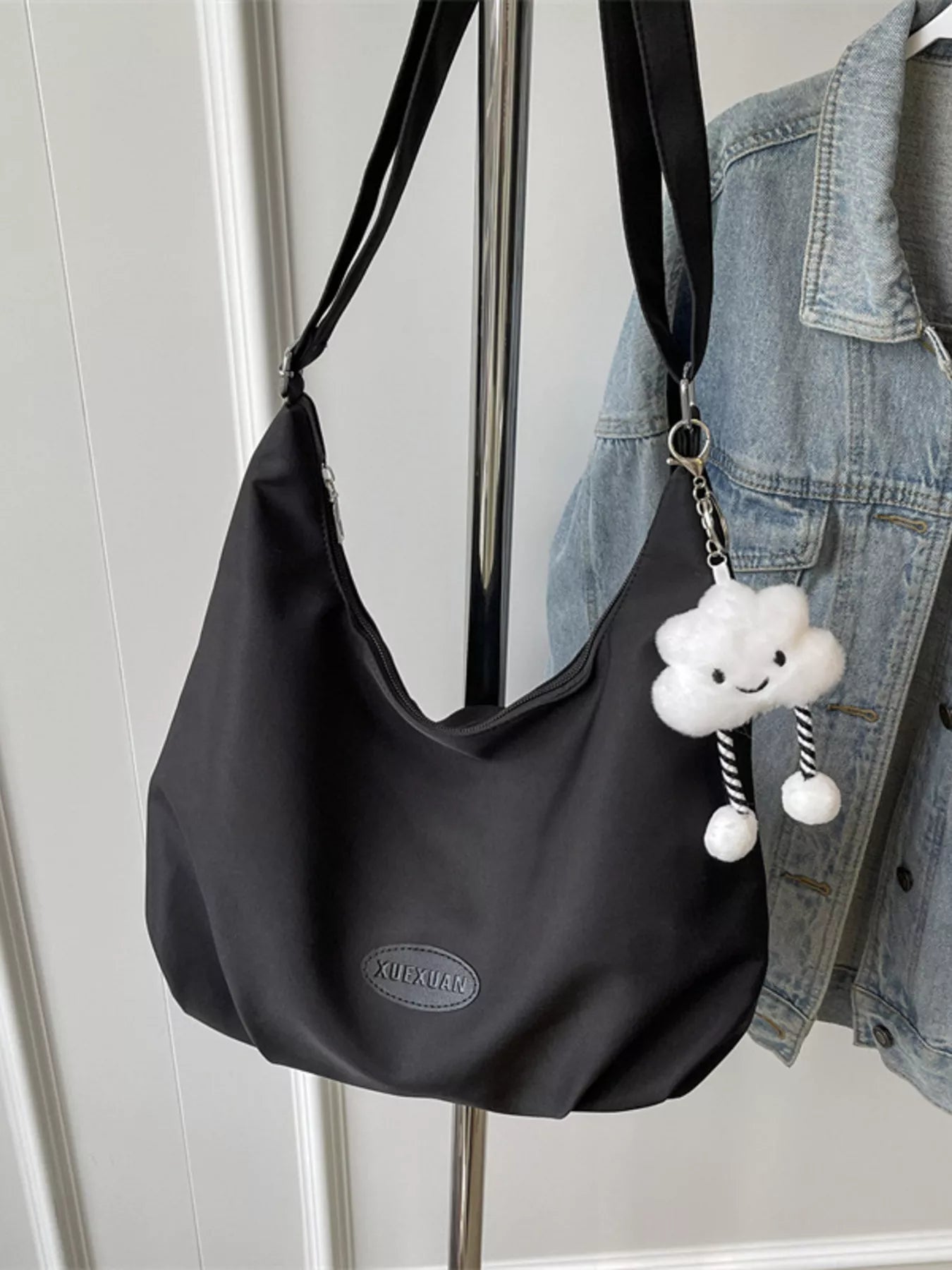 Black shoulder bag with a cloud-shaped keychain on a hanger against a white wall.