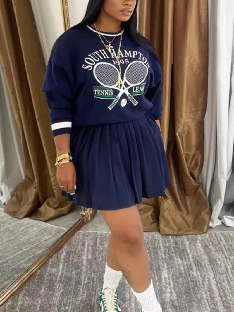 Person wearing a navy blue sweatshirt with tennis graphics and a matching skirt indoors.