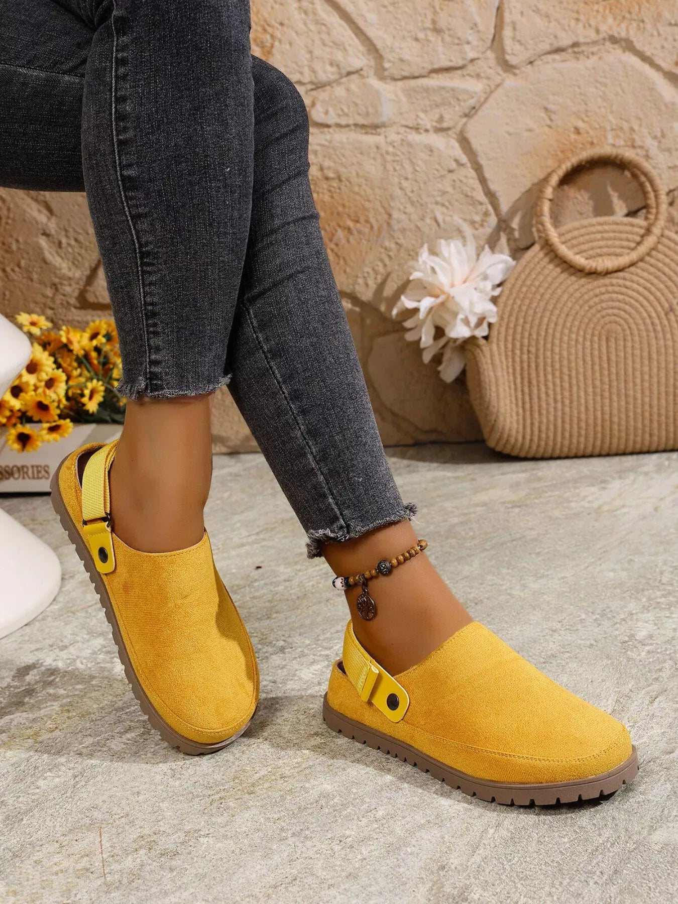 Yellow suede clogs worn with dark jeans against a stone wall background