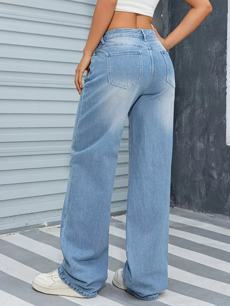 Person wearing light blue jeans standing against a striped floor and gray wall.
