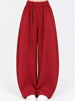 A pair of wide-leg, balloon-style pants in a deep red or burgundy color, featuring an elastic waistband with hanging drawstrings, shown on a model from the waist down against a plain white background.