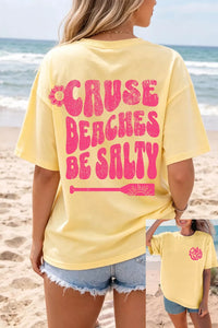 Person wearing a yellow t-shirt with pink text on a beach