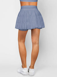 Person wearing a blue tennis skirt and white sneakers on a light gray background