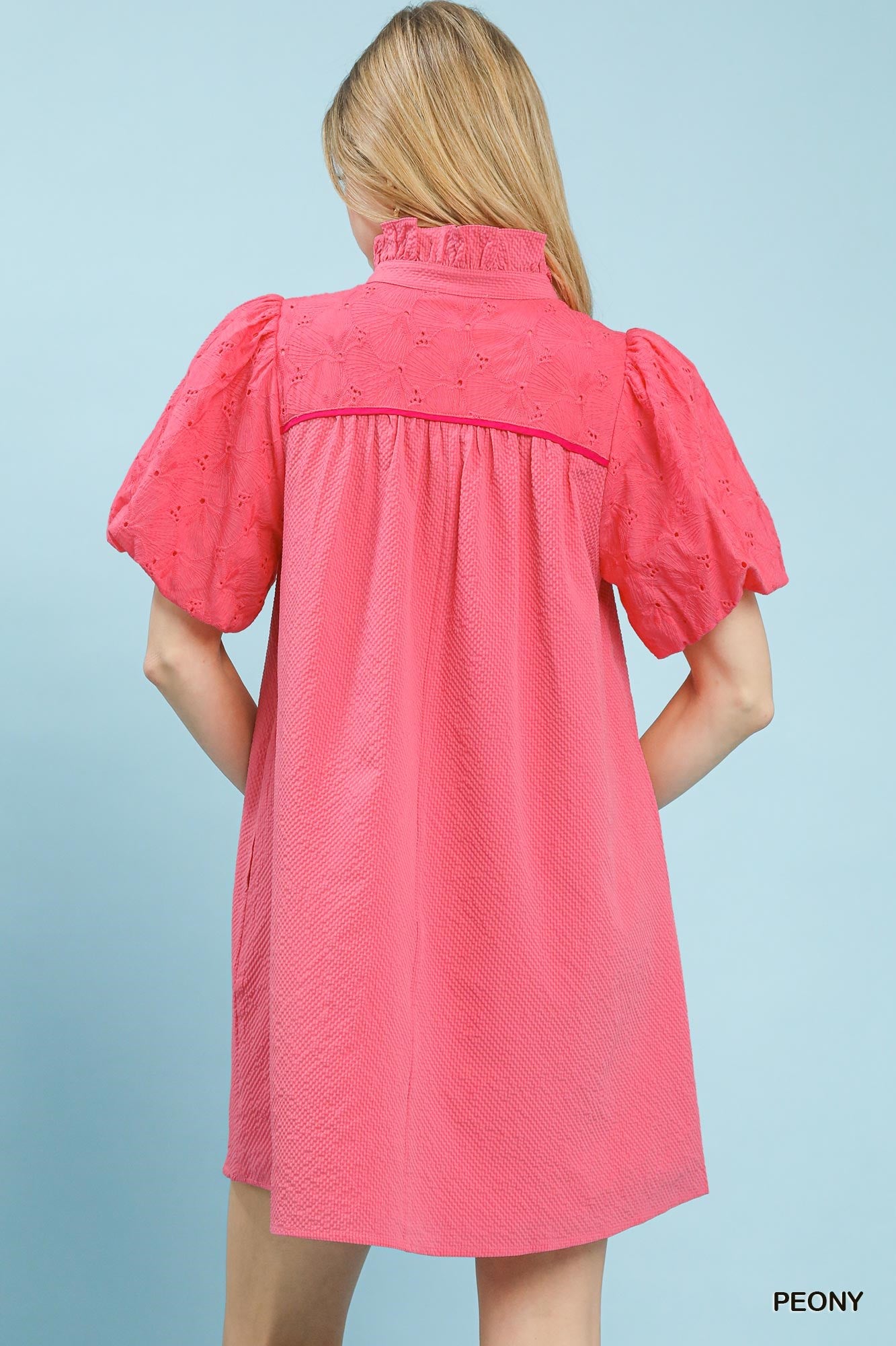 Woman wearing a pink dress with puff sleeves against a light blue background