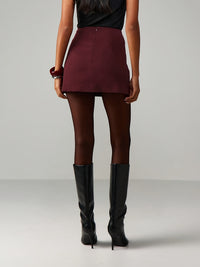 Person wearing a burgundy mini skirt and black knee-high boots on a plain background