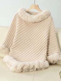 Beige knitted poncho with fur trim on a hanger against a light background