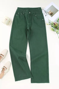 Green pants on a white surface with a cup and plant in the background