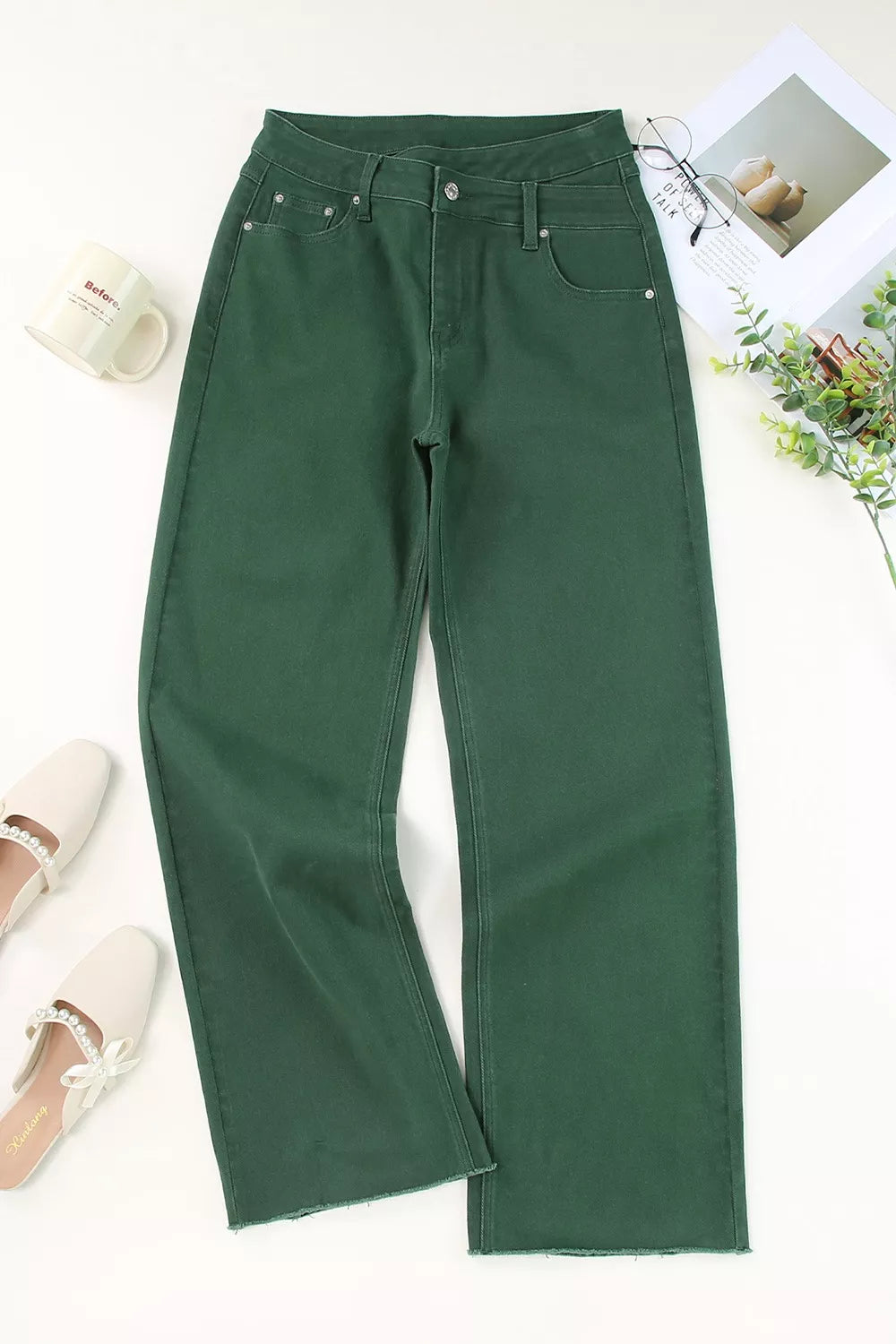 Green pants on a white surface with a cup and plant in the background