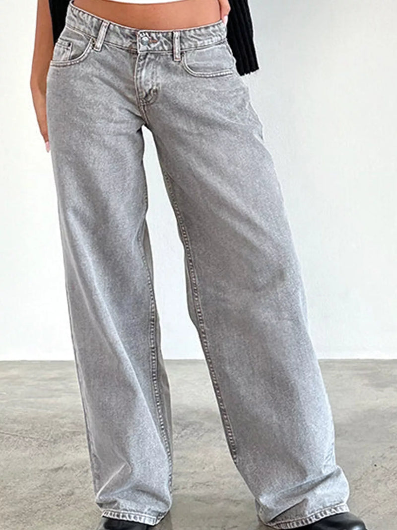 A person wearing light gray wide-leg denim jeans, shown from the waist down against a plain light wall and concrete floor.