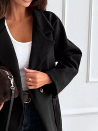 Person wearing a black coat over a white top, holding a brown leather bag.