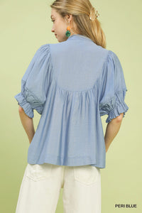 Woman wearing a light blue blouse with ruffled sleeves on a green background