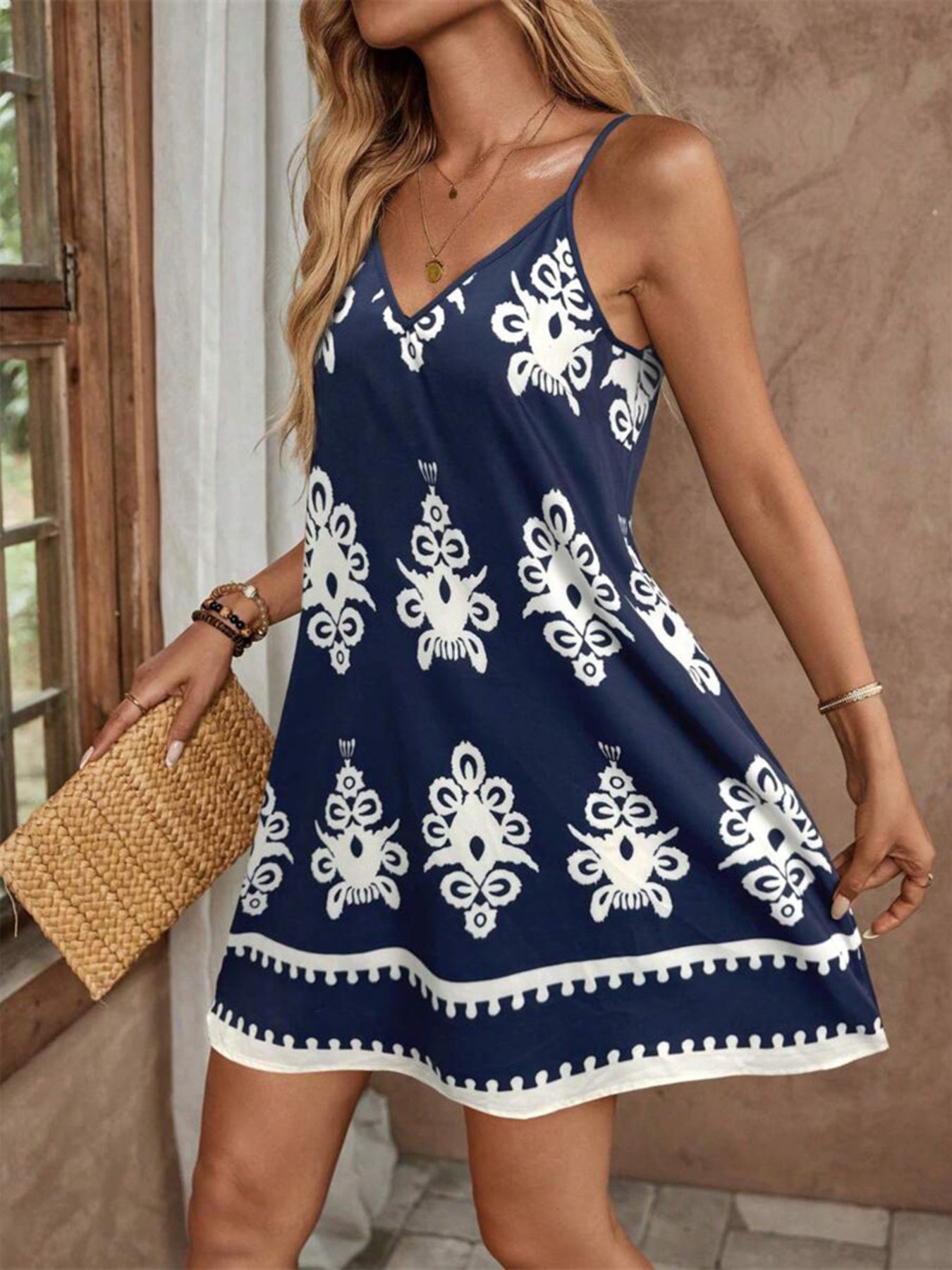Woman wearing a navy blue dress with white patterns, holding a straw bag indoors.
