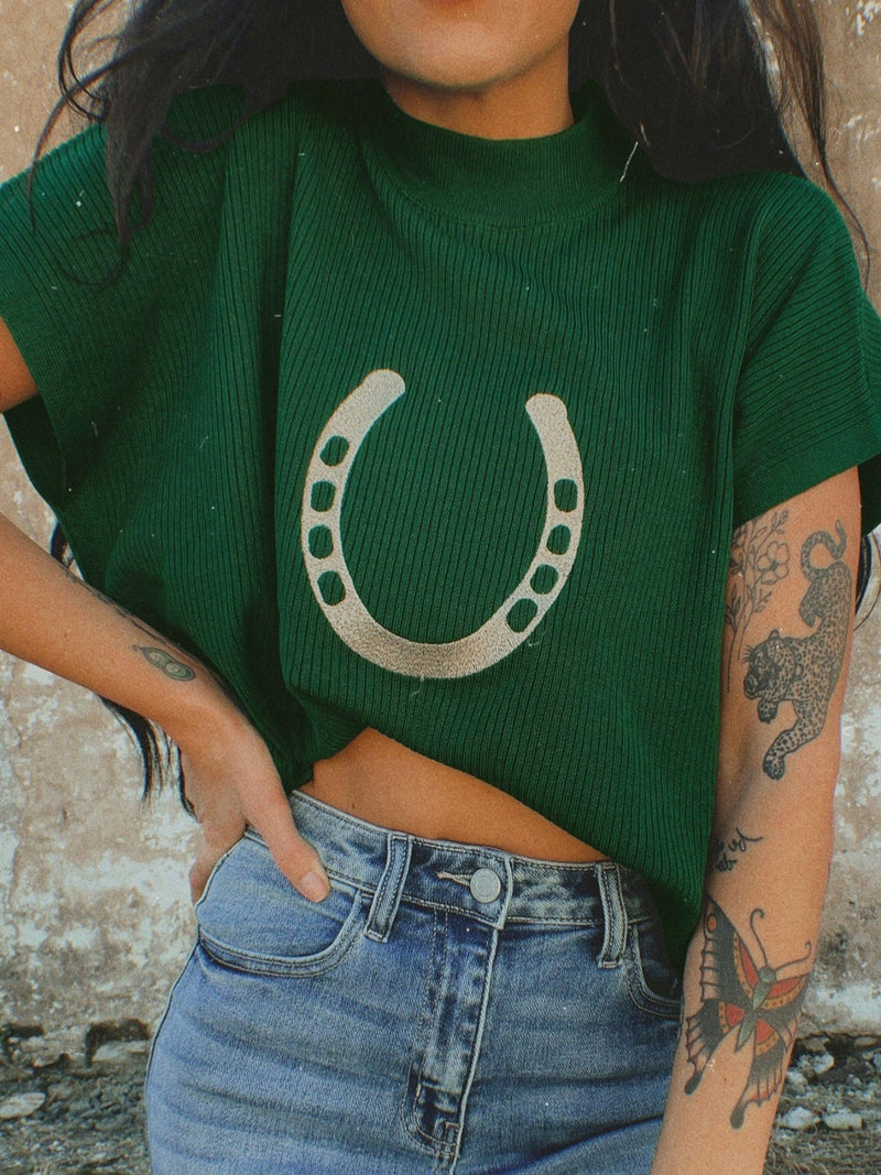 Person wearing a green sweater with a horseshoe design and blue jeans.