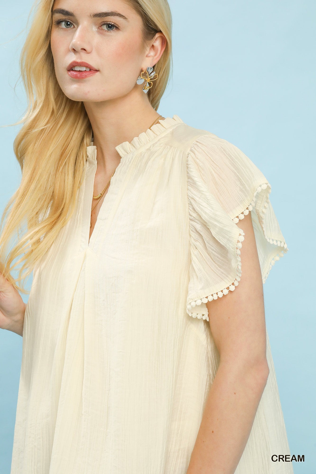 Woman wearing a cream-colored blouse with ruffled sleeves against a light blue background
