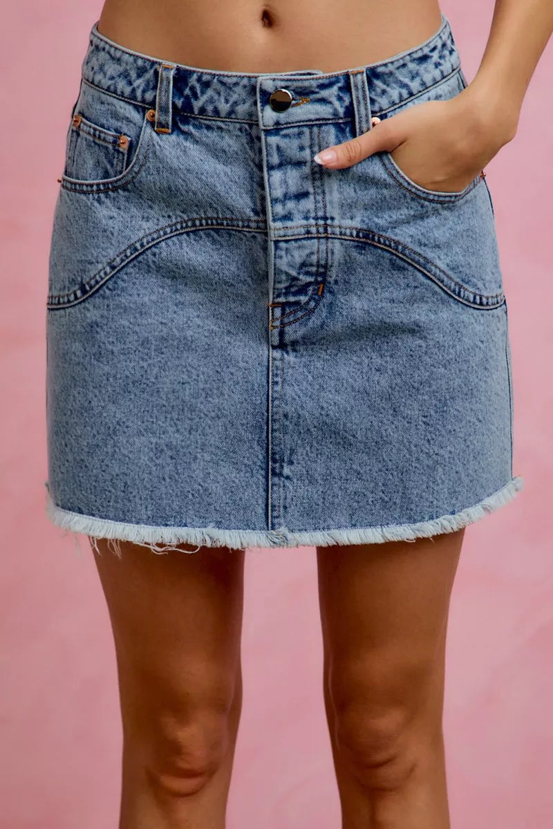 Blue denim skirt worn by a person on a pink background