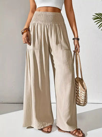 Person wearing beige wide-leg pants holding a woven bag on a white background