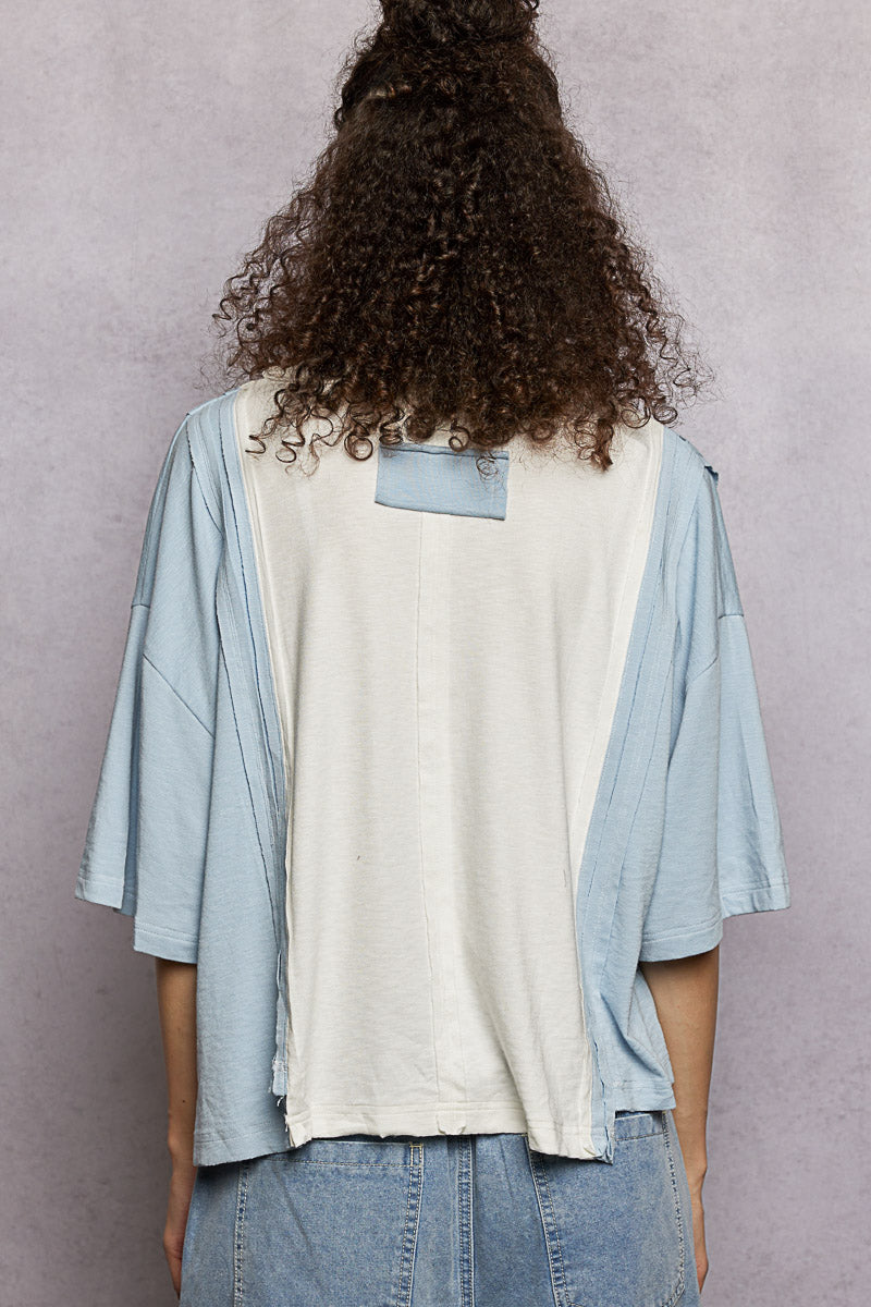 Person wearing a light blue kimono-style garment over a white shirt with a pocket, standing against a plain background.