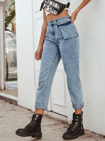 Person wearing light blue jeans and black boots standing against a white wall.